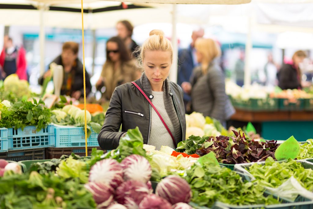 Woman buying fruits and vegetables at local food market. Market stall with variety of organic vegetable.